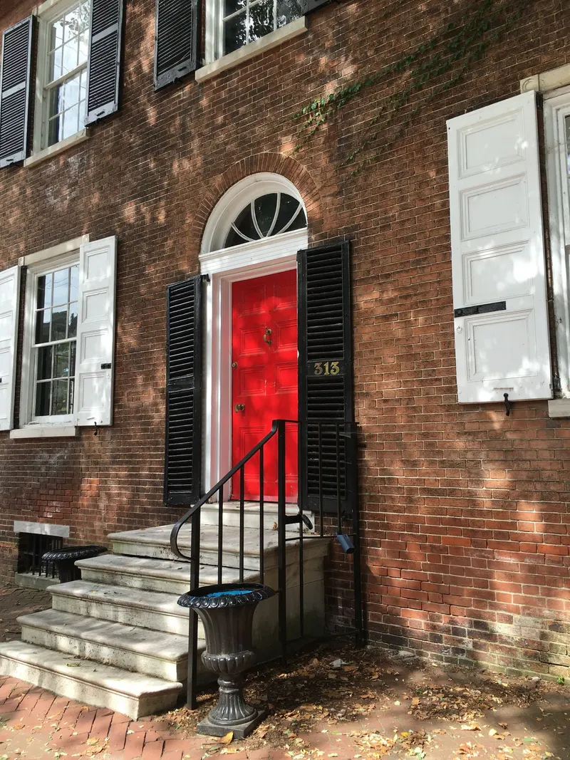 Unpainted red brick facade with a painted red front door, white window trim and black shutters